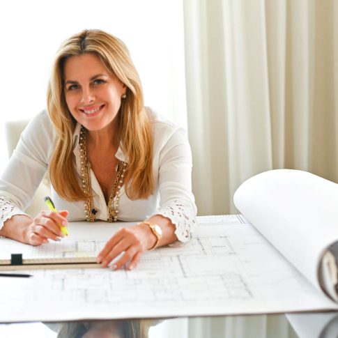 Maura Rossi, an accomplished interior designer, standing in a stylishly decorated living room she designed, exemplifying her elegant and innovative aesthetic.