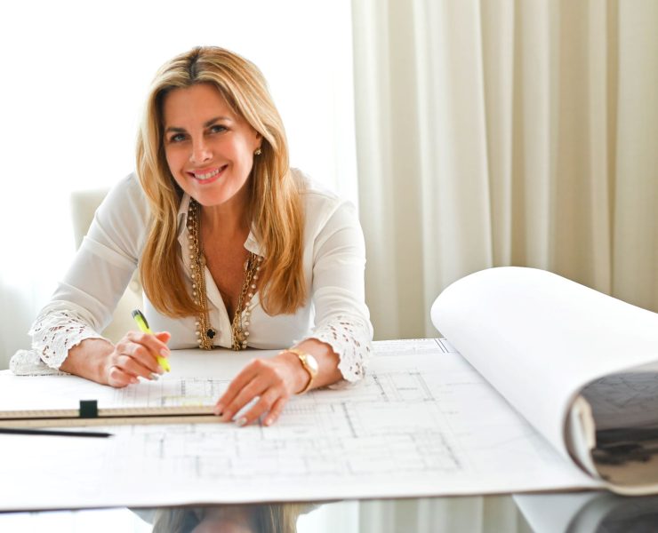 Maura Rossi, an accomplished interior designer, standing in a stylishly decorated living room she designed, exemplifying her elegant and innovative aesthetic.