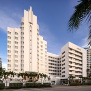Iconic Art Deco-style luxury hotel in Miami Beach surrounded by palm trees and ocean views. Caption: Miami Beach’s timeless Art Deco charm — a blend of heritage architecture and modern sophistication.