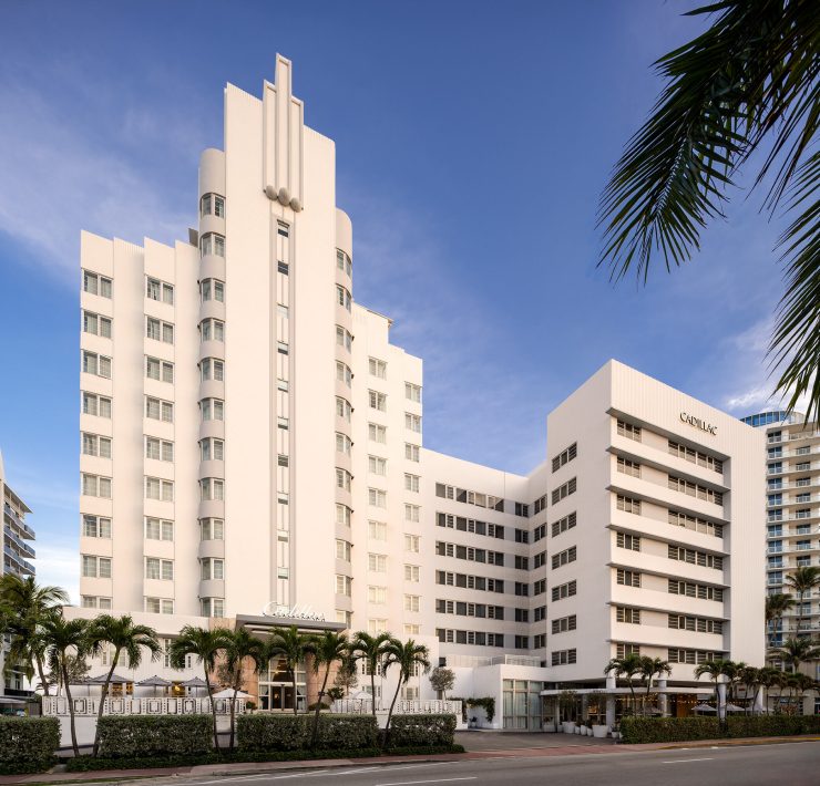 Iconic Art Deco-style luxury hotel in Miami Beach surrounded by palm trees and ocean views. Caption: Miami Beach’s timeless Art Deco charm — a blend of heritage architecture and modern sophistication.