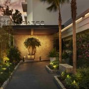 Illuminated entrance to The Gates Hotel South Beach with lush greenery and evening ambiance. Caption: The Gates Hotel welcomes guests through a serene, tropical-inspired entrance just steps from the beach.
