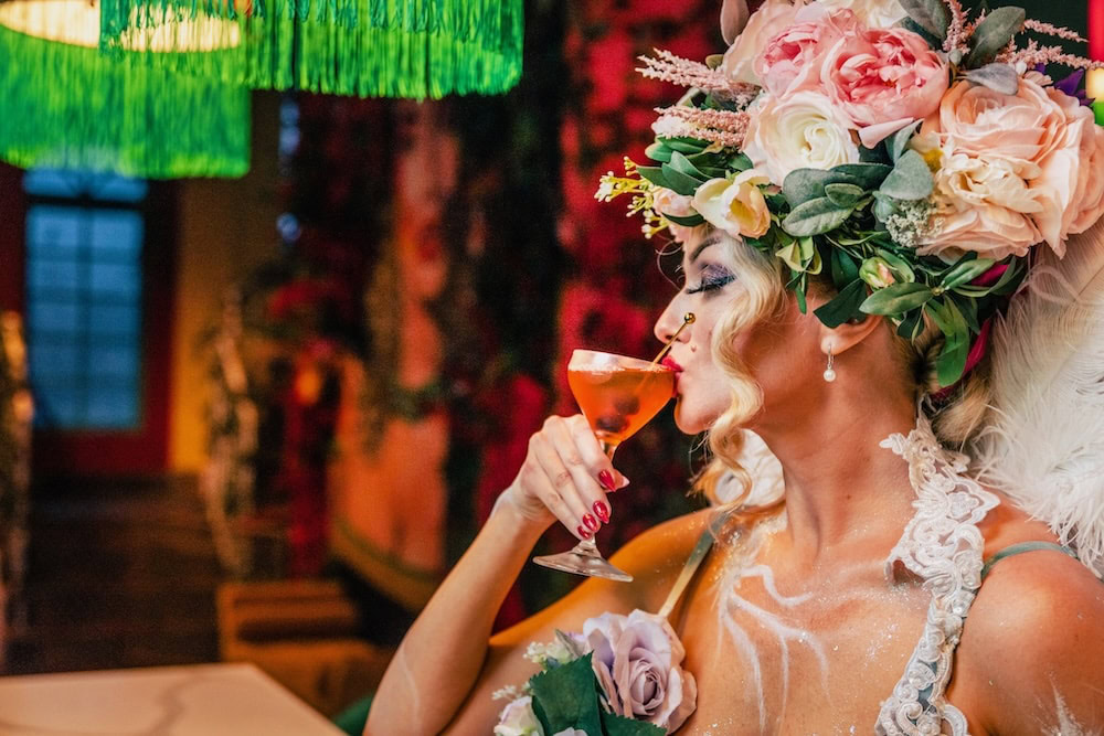 Woman in floral costume sipping a Halloween-themed cocktail at a Miami restaurant during spooky season.