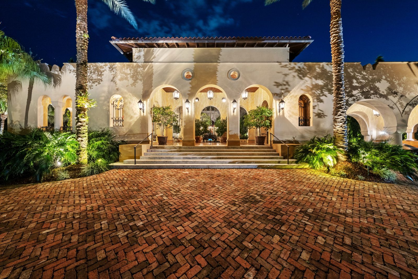 Luxury Mediterranean-style Coral Gables estate entrance designed by developer Armando Codina, featuring arched columns and lush landscaping.