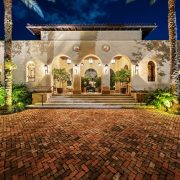 Luxury Mediterranean-style Coral Gables estate entrance designed by developer Armando Codina, featuring arched columns and lush landscaping.