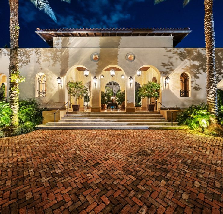 Luxury Mediterranean-style Coral Gables estate entrance designed by developer Armando Codina, featuring arched columns and lush landscaping.