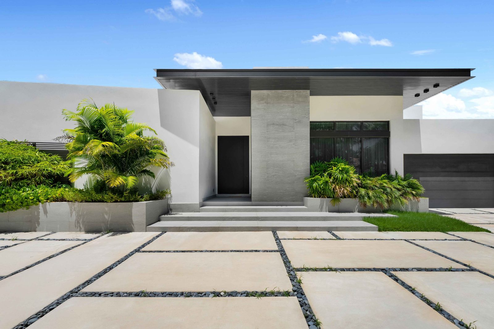 Exterior view of the modern single-story home in Golden Beach with minimalist architecture, landscaped entryway, and sleek stone detailing.
