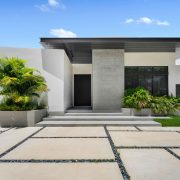 Exterior view of the modern single-story home in Golden Beach with minimalist architecture, landscaped entryway, and sleek stone detailing.