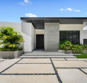 Exterior view of the modern single-story home in Golden Beach with minimalist architecture, landscaped entryway, and sleek stone detailing.