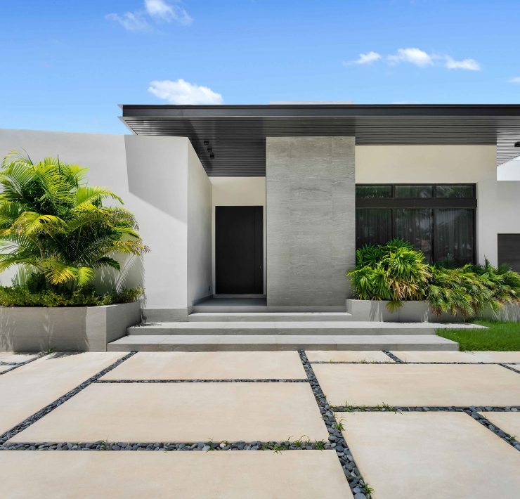 Exterior view of the modern single-story home in Golden Beach with minimalist architecture, landscaped entryway, and sleek stone detailing.