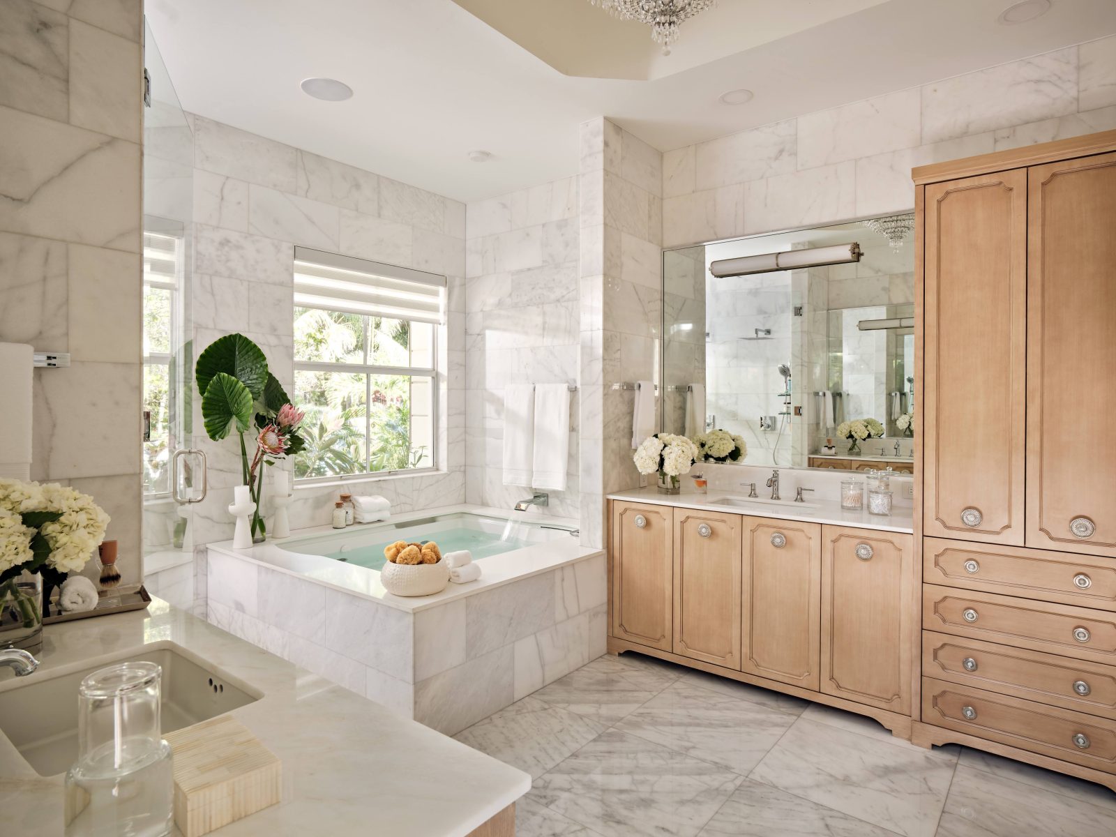 Luxury primary bathroom featuring marble surfaces, soaking tub, and warm wood cabinetry designed by Maritza Capiro.