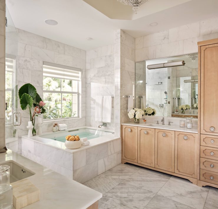 Luxury primary bathroom featuring marble surfaces, soaking tub, and warm wood cabinetry designed by Maritza Capiro.