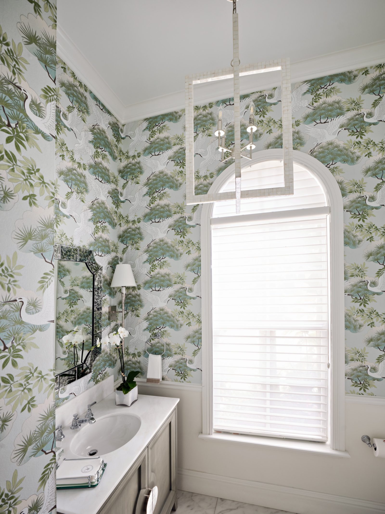 Powder room featuring botanical wallpaper, white vanity, and large arched window.