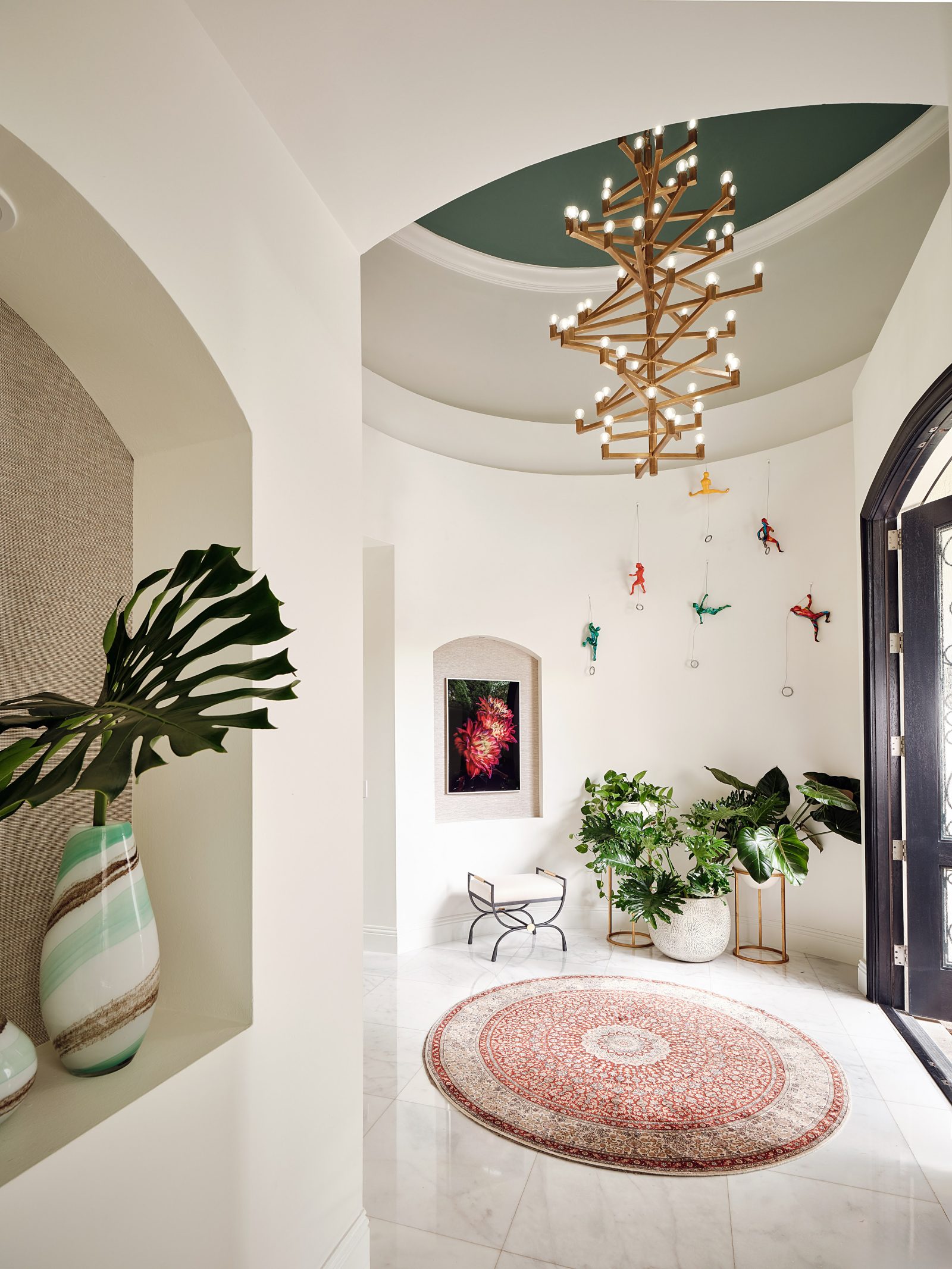 “Elegant foyer with sculptural chandelier, marble floors, and arched entry designed by Maritza Capiro