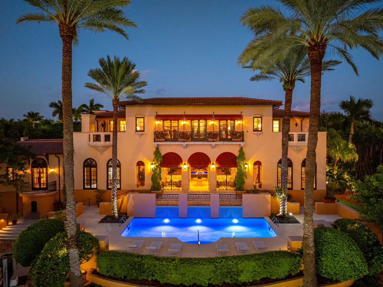 Rear exterior of Armando Codina’s Coral Gables mansion featuring resort-style pool, palm trees, and sunset ambiance.
