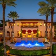 Rear exterior of Armando Codina’s Coral Gables mansion featuring resort-style pool, palm trees, and sunset ambiance.