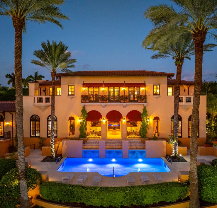 Rear exterior of Armando Codina’s Coral Gables mansion featuring resort-style pool, palm trees, and sunset ambiance.