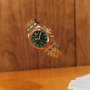 Gold Versace FW25 watch with a green dial suspended midair, showcasing bold elegance.