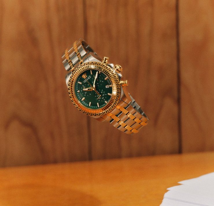 Gold Versace FW25 watch with a green dial suspended midair, showcasing bold elegance.