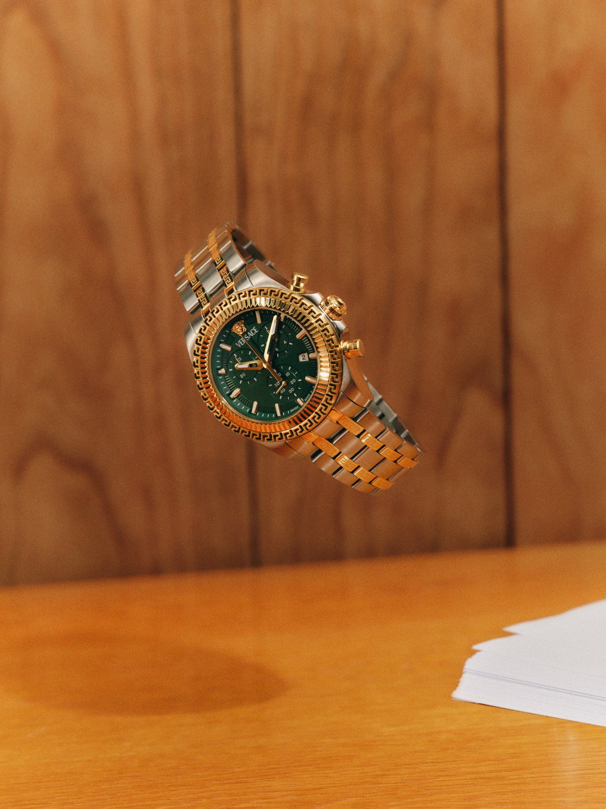Gold Versace FW25 watch with a green dial suspended midair, showcasing bold elegance.