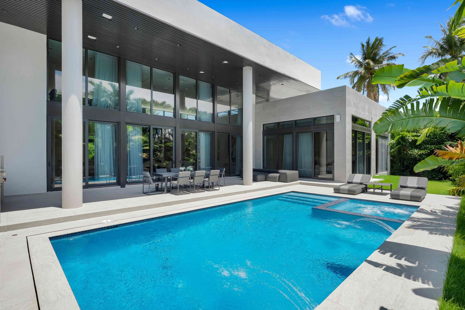 Modern outdoor pool with jacuzzi, terrace seating, and tropical landscaping at a luxury home in Golden Beach, Florida.