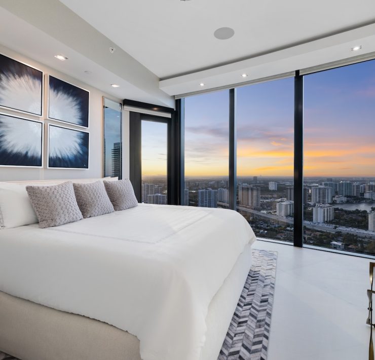 Elegant master bedroom at Porsche Design Tower Penthouse 4405 showcasing floor-to-ceiling glass and panoramic sunset views over Miami.