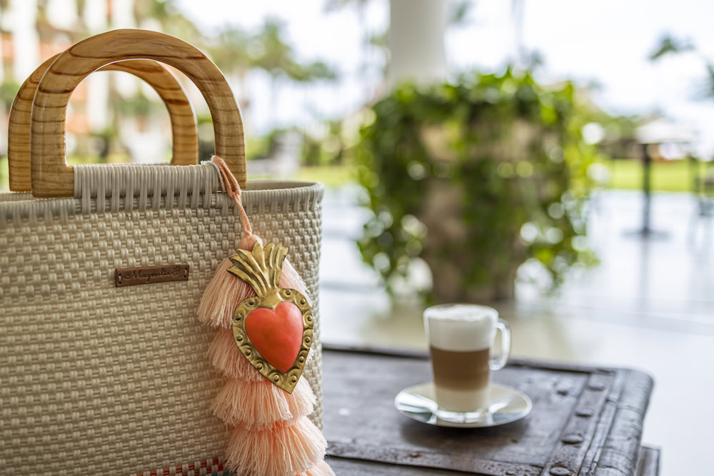 Handcrafted woven bag with tassel decoration beside a coffee cup at a luxury resort.