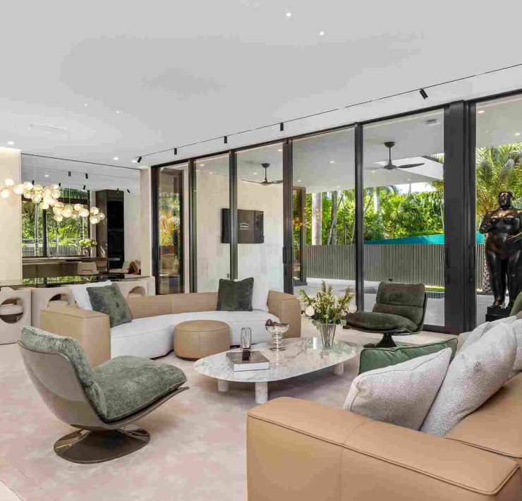 Living room of luxury estate on Sunset Islands featuring floor-to-ceiling windows, neutral décor, and tropical garden views.