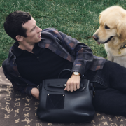 Man lying on grass with golden retriever and Louis Vuitton LV Touch black leather bag.
