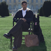 Model sitting on a chair with black dog and Louis Vuitton LV Touch Steamer bag on green lawn.