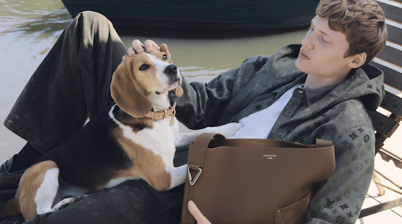 Man relaxing outdoors with a beagle and Louis Vuitton LV Touch brown leather bag.