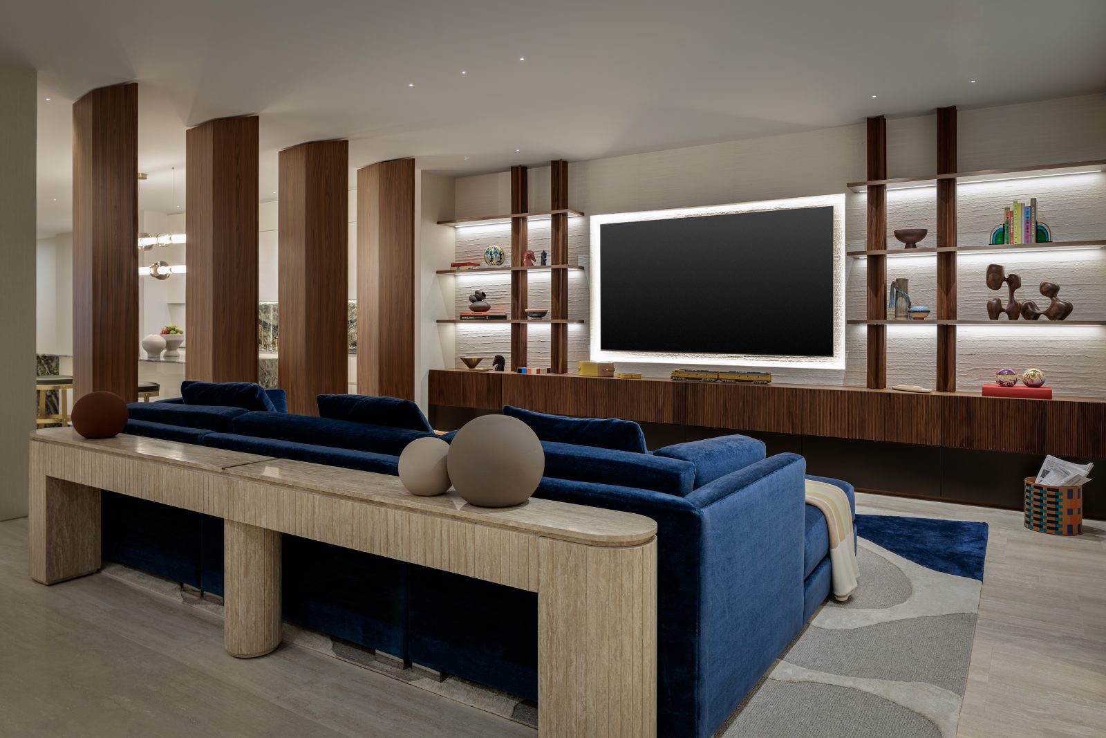 Contemporary media room designed by Genevieve Lake featuring navy velvet seating, wood panel accents, and built-in shelving.