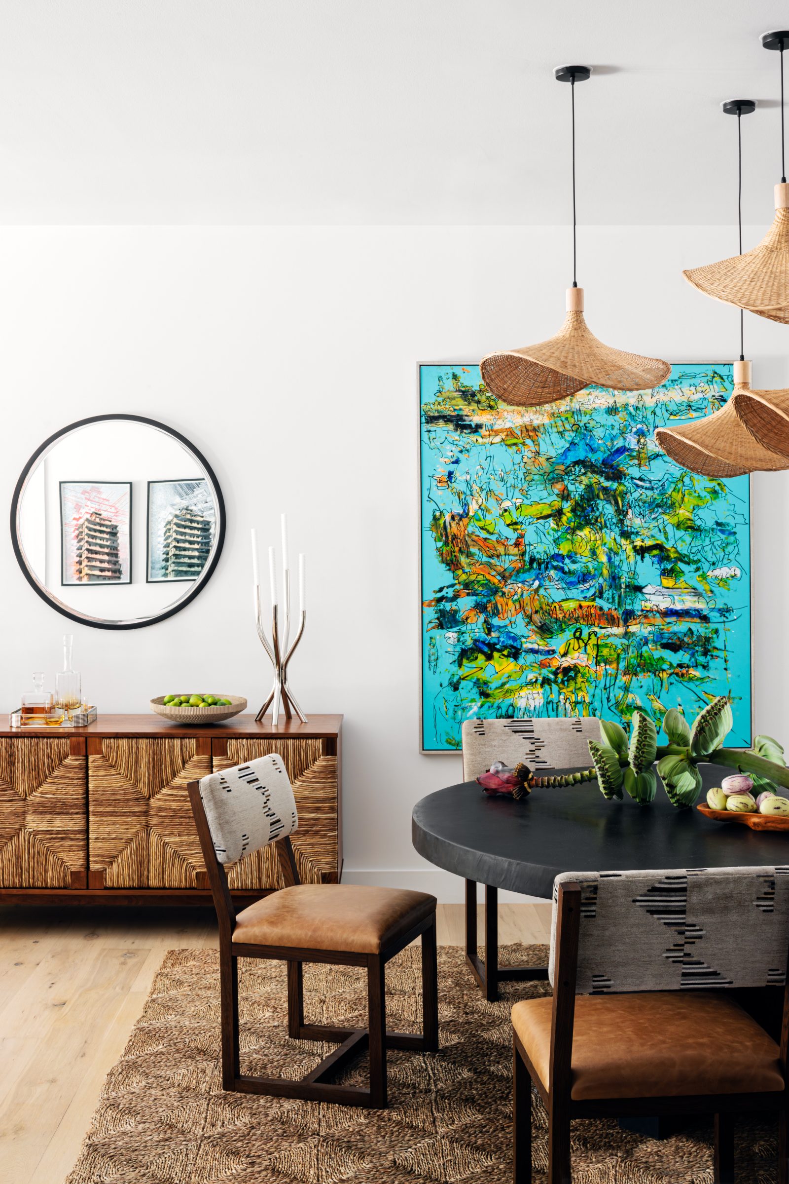 Miami bungalow dining room designed by Genevieve Lake featuring a round black table, woven pendant lights, and colorful contemporary artwork.