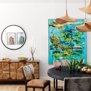 Miami bungalow dining room designed by Genevieve Lake featuring a round black table, woven pendant lights, and colorful contemporary artwork.