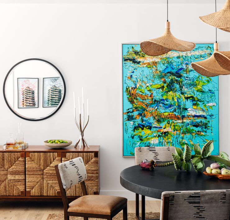 Miami bungalow dining room designed by Genevieve Lake featuring a round black table, woven pendant lights, and colorful contemporary artwork.