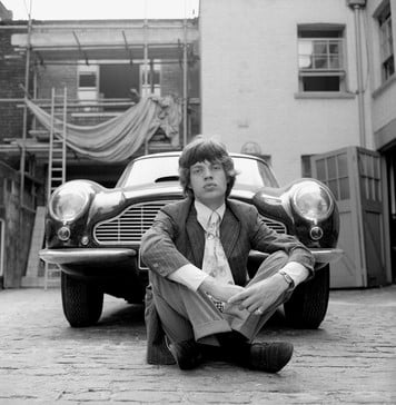 Black-and-white portrait of Mick Jagger seated in front of a classic car, part of The Betsy’s Art Week photography collection.