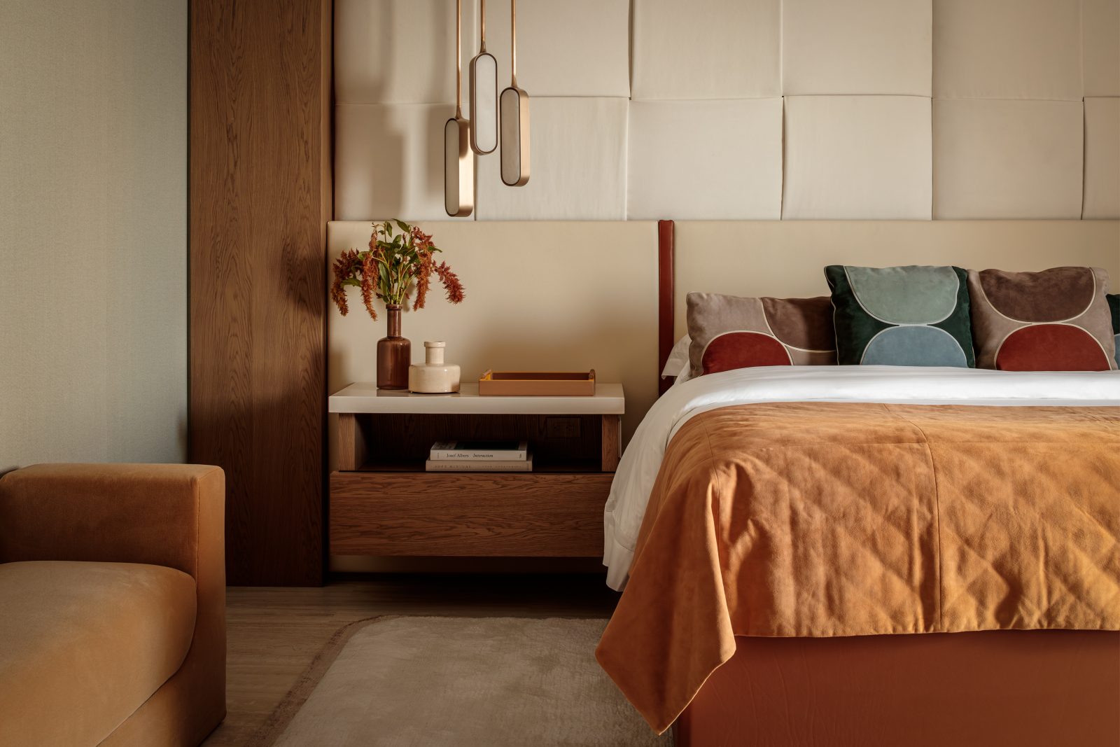 Primary bedroom designed by Genevieve Lake featuring warm earth tones, upholstered headboard, and modern pendant lighting.