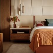 Primary bedroom designed by Genevieve Lake featuring warm earth tones, upholstered headboard, and modern pendant lighting.