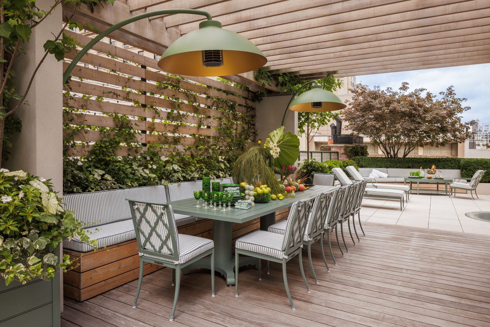 Rooftop terrace designed by Genevieve Lake featuring outdoor dining area, greenery, and modern pergola with pendant lighting.