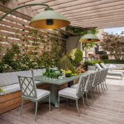 Rooftop terrace designed by Genevieve Lake featuring outdoor dining area, greenery, and modern pergola with pendant lighting.