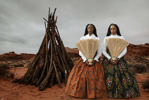 Portrait-style artistic photograph of two women in traditional-inspired attire with fans, exhibited for Miami Art Week.