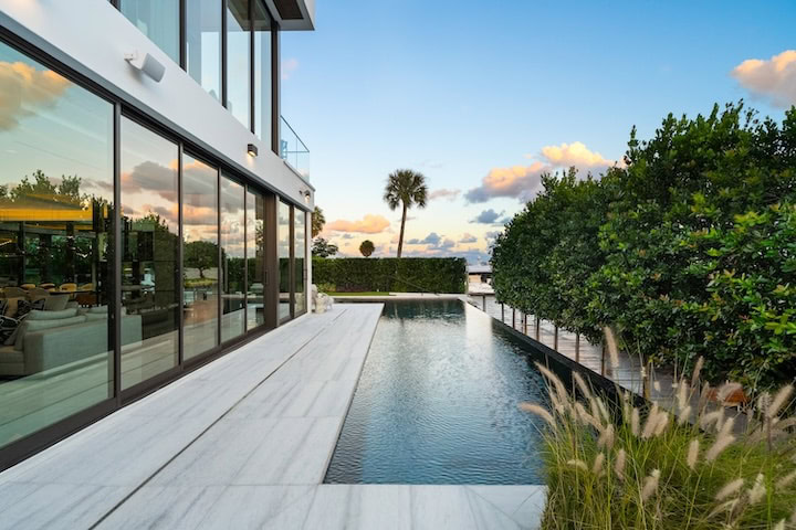 Heated infinity pool and terrace with sleek marble finishes and tropical landscaping at Casa Moderne, Bay Point, Miami.