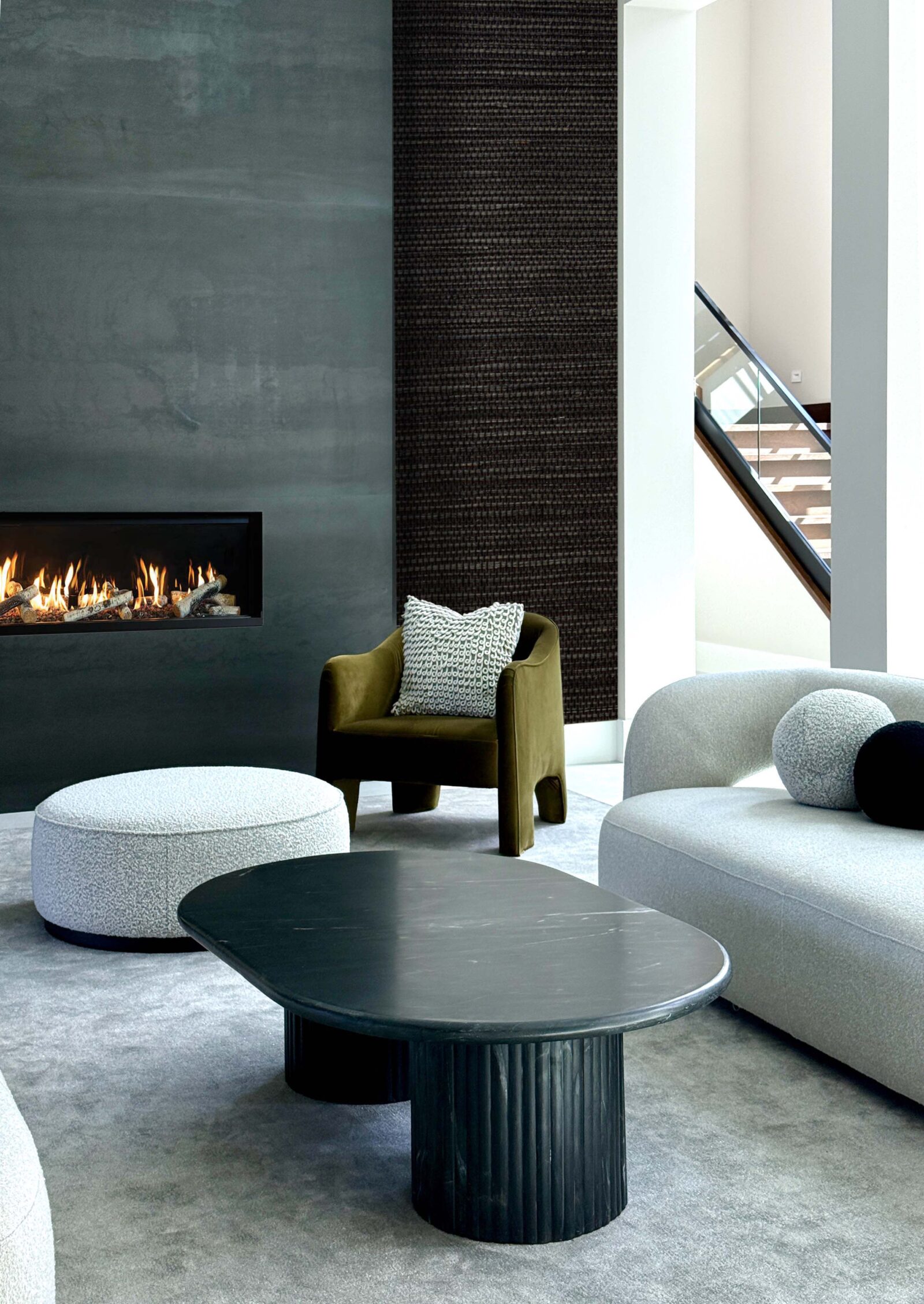 Modern luxury living room by Deborah Gregg Interiors featuring a sleek black fireplace wall, sculptural curved seating, a black statement coffee table, and a textured accent wall with soft neutral tones.