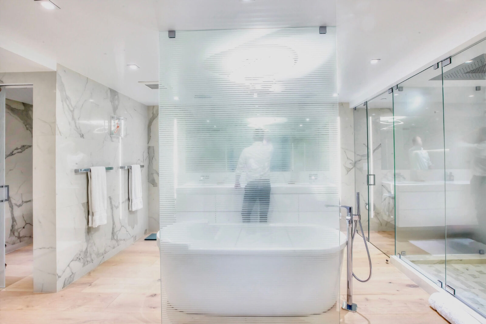 Modern spa-like bathroom with marble walls, frosted glass partition, freestanding tub, and glass shower enclosure
