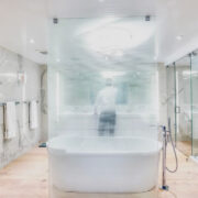Modern spa-like bathroom with marble walls, frosted glass partition, freestanding tub, and glass shower enclosure