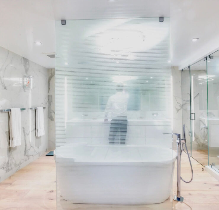 Modern spa-like bathroom with marble walls, frosted glass partition, freestanding tub, and glass shower enclosure
