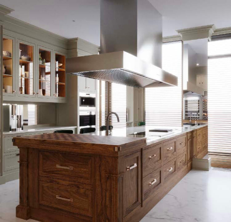 Refined kitchen with taupe cabinetry, rich wood island, marble flooring, and oversized stainless steel hood