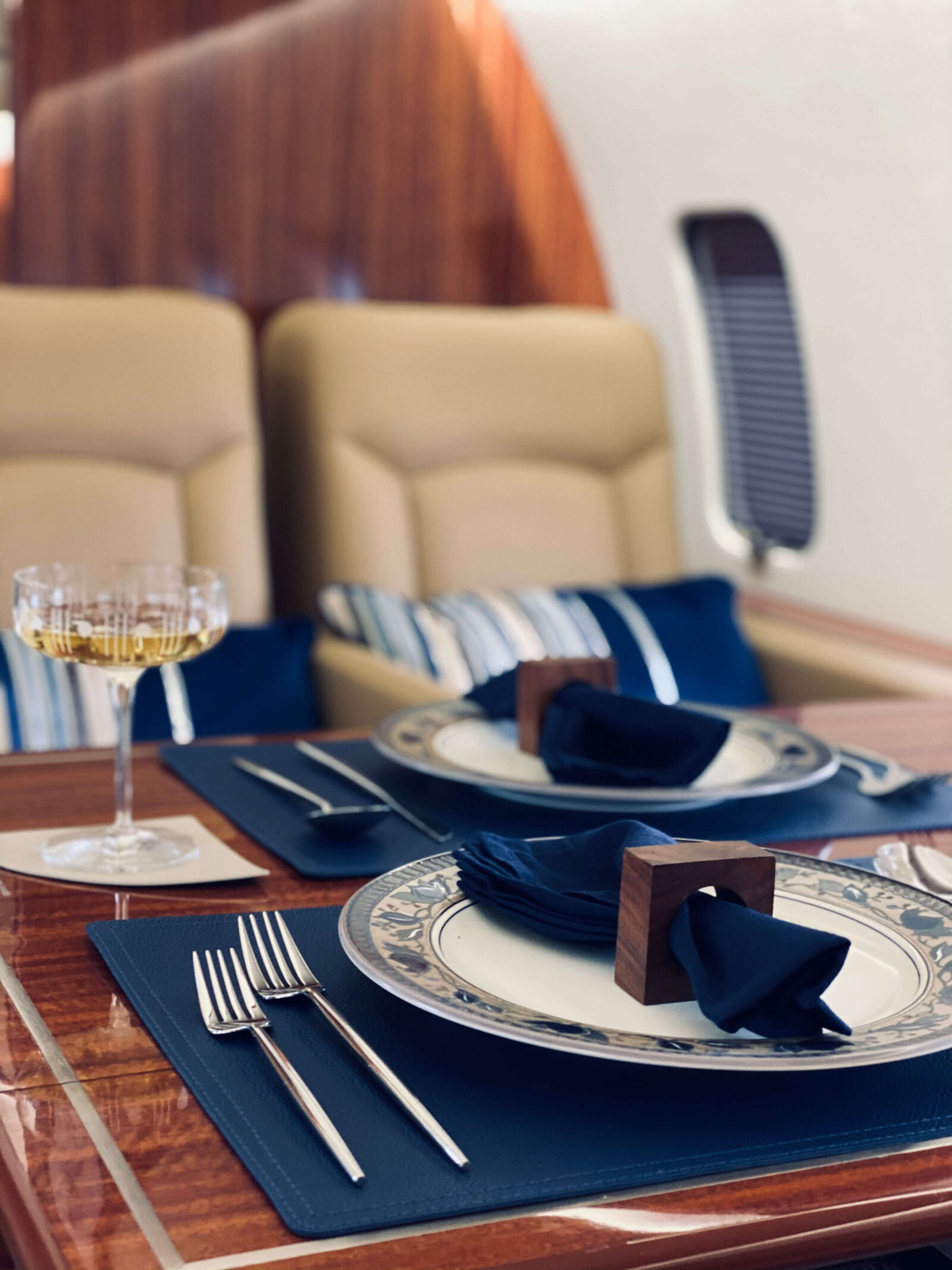 Private jet dining setup with polished wood table, navy linens, fine china, and champagne glass