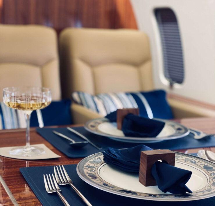 Private jet dining setup with polished wood table, navy linens, fine china, and champagne glass