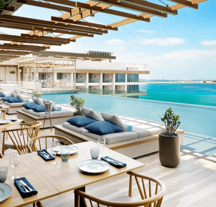 Luxury poolside terrace with ocean views, daybeds, dining tables, and airy resort-style architecture