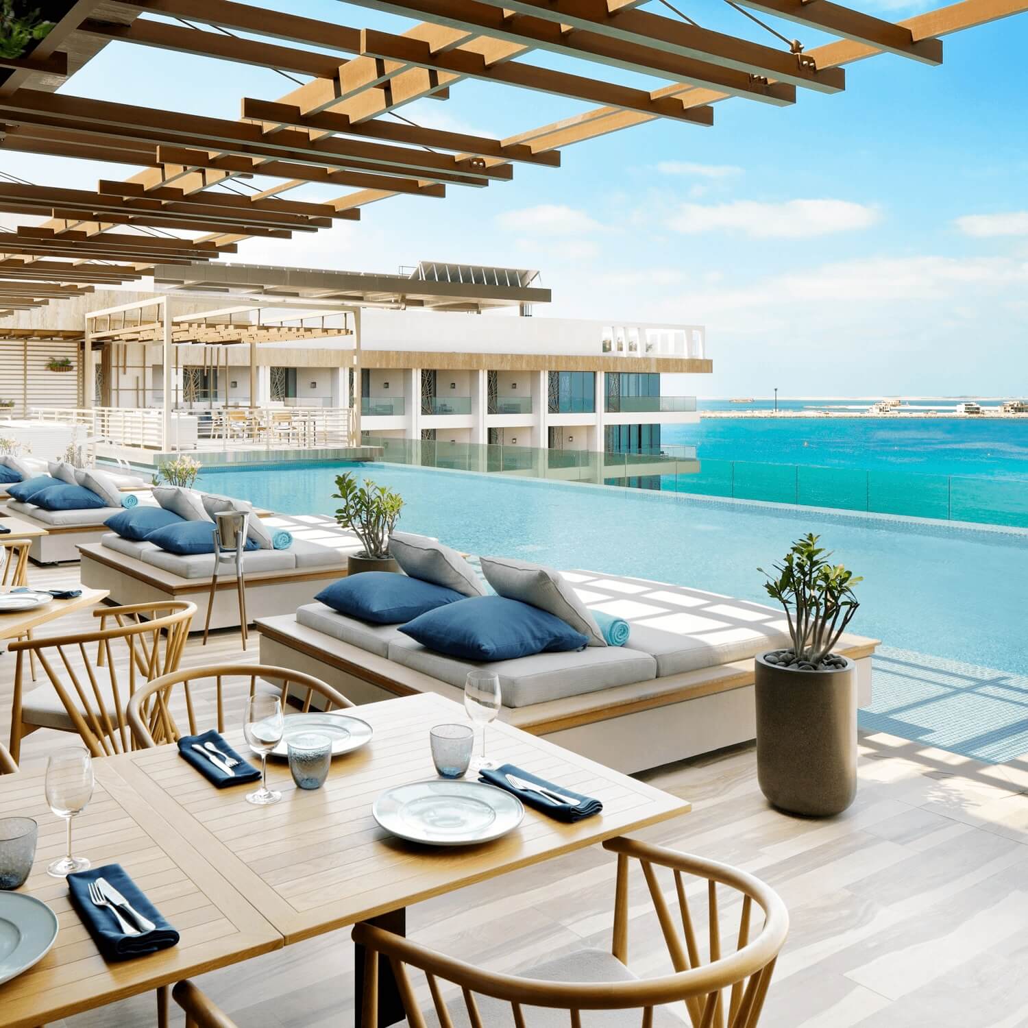 Luxury poolside terrace with ocean views, daybeds, dining tables, and airy resort-style architecture